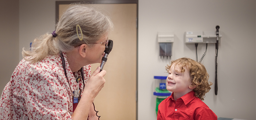 A doctor examines a young child with curly hair sitting on bed at a clinic.