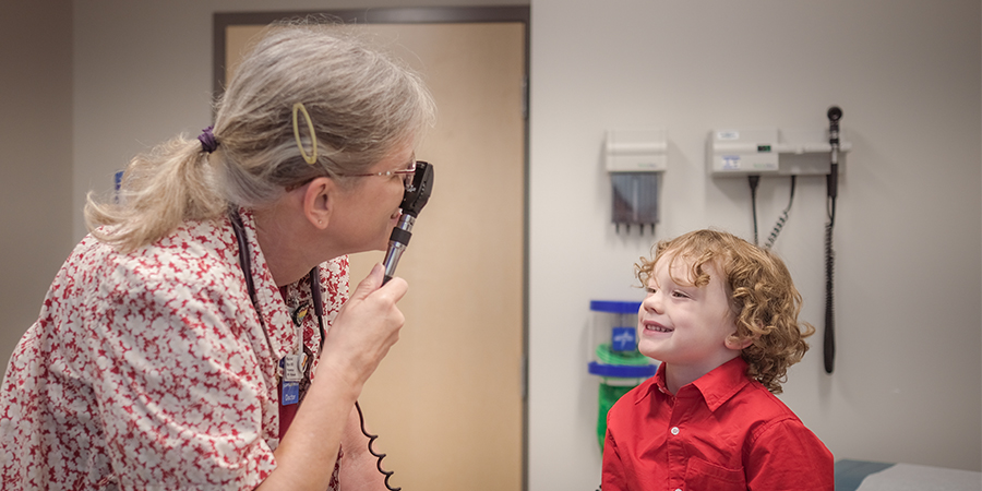 A doctor examines a young child with curly hair sitting on bed at a clinic.